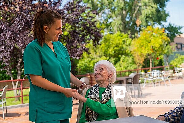 Eine ältere oder reife Frau mit einer Krankenschwester im Garten eines Pflegeheims in einem Moment der Zuneigung
