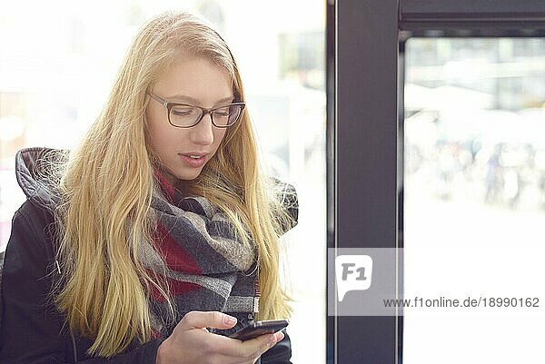 Konzentrierte blonde Frau  die eine Nachricht auf ihrem Mobiltelefon liest  während sie in einem Bus sitzt  Konzept für öffentliche Verkehrsmittel und Technologie
