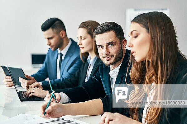Porträt einer lächelnden Gruppe von Geschäftsleuten  die in einer Reihe zusammen am Tisch in einem modernen Büro sitzen. Business Team Konzept