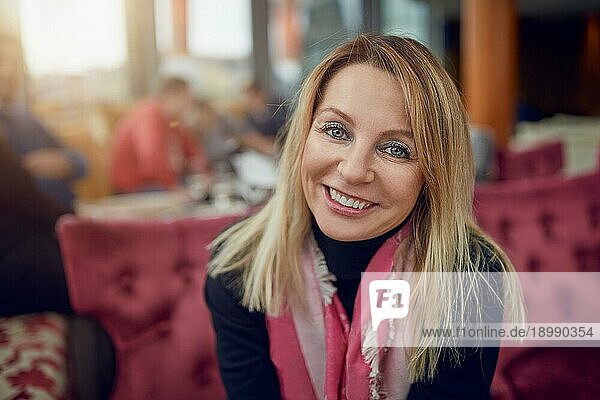 Attraktive Frau mittleren Alters  die in einem Restaurant sitzt und in die Kamera lächelt