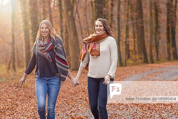 Zwei fröhliche Frauen  die Hand in Hand durch einen bewaldeten Herbstpark laufen  in dem bunte Blätter auf dem Boden liegen ein Konzept für einen gesunden Lebensstil