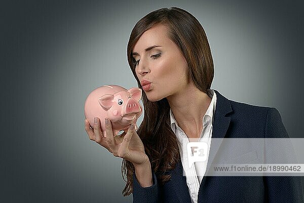 Erfolgreiche Geschäftsfrau  die ihr Sparschwein küsst  während sie ihren geschäftlichen Erfolg und ihre Fähigkeit  für eine sichere Zukunft zu sparen oder ein Vermögen anzuhäufen  feiert