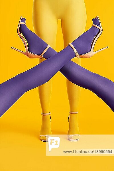 Lange schlanke gekreuzte Beine junger Frauen in lila Strumpfhosen  die auf einer Frau in gelben Strumpfhosen posieren. Pop Art  weibliches Konzept