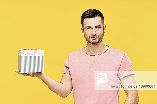 Hübscher junger Mann hält Geschenkbox auf gelbem Studio Hintergrund. Feiern  Geschenkkonzept