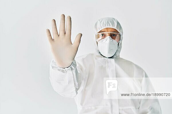 Arzt im medizinischen Schutzanzug zeigt Stoppschild auf weißem Hintergrund. Verbotssymbol