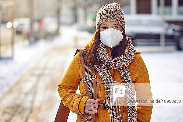 Brünette Frau mittleren Alters in Winterkleidung trägt auf dem Weg zur Arbeit eine Gesichtsmaske wegen des Coronavirus im Freien