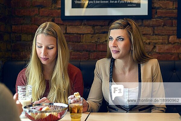 Drei attraktive  junge  stilvolle Frauen essen und trinken zusammen in einem Restaurant  sitzen an einem Tisch  essen und unterhalten sich