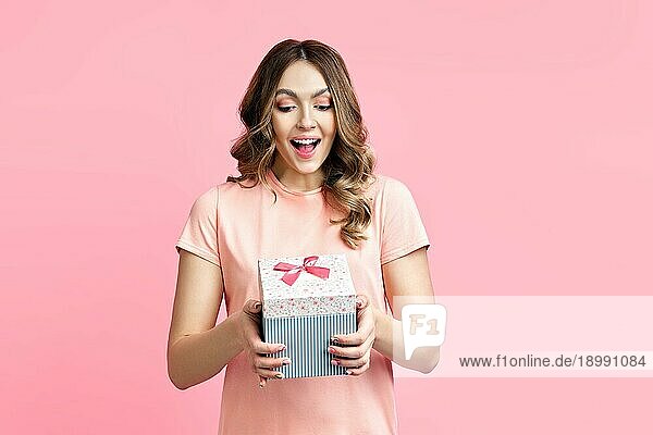 Excited lächelnde Frau Frau hält Geschenkbox über rosa Hintergrund. Geschenk  Überraschung  Feier Konzept