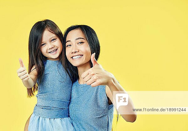 Glückliche Mutter und ihr Kind Tochter zeigt Daumen hoch und haben Spaß zusammen auf gelbem Hintergrund. Familie  Motivation Konzept
