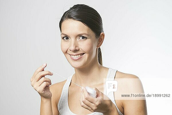 Frau  die ihre Zähne mit Zahnseide reinigt  um Speisereste und Bakterien zwischen den Zähnen zu entfernen und so Karies vorzubeugen