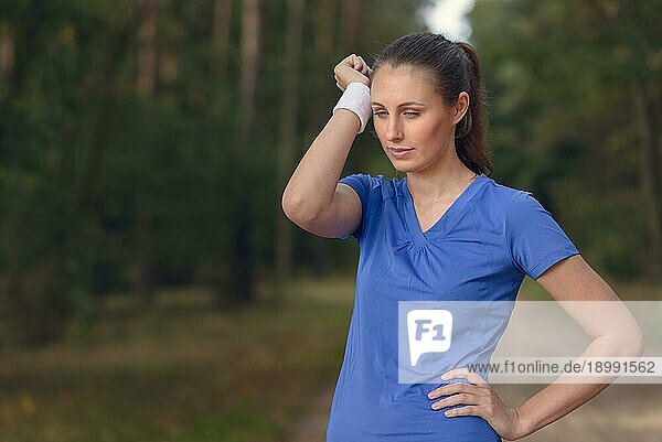 Eine Sportlerin wischt sich den Schweiß von der Stirn auf ihr Armband  als sie während ihrer Trainingsübungen auf einem Waldweg eine Pause einlegt