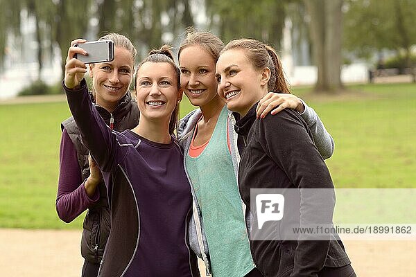 Halbkörperaufnahme von vier glücklichen Frauen  die ein Selfie mit ihrem Smartphone machen  nachdem sie eine körperliche Übung im Freien im Park gemacht haben