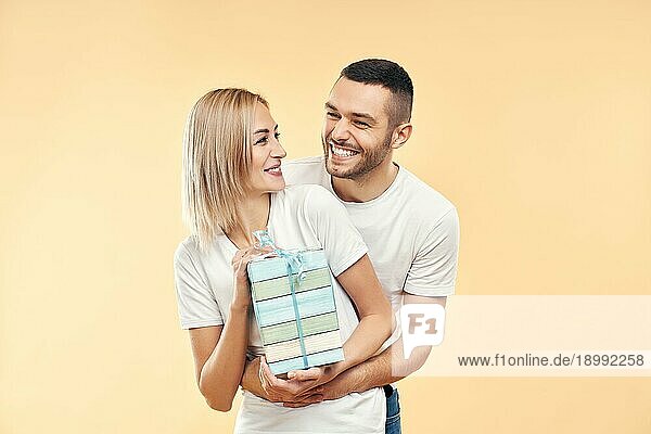 Junges glückliches Paar mit Geschenkbox über beige Hintergrund. Geschenk  Urlaub  Feier Konzept