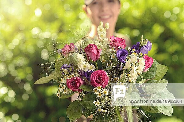 Frau im Garten  die der Kamera einen Strauß verschiedener frischer Blumen in Nahaufnahme anbietet