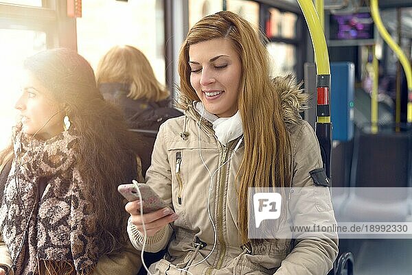 Glückliche blonde Frau  die eine Nachricht auf ihrem Mobiltelefon liest  während sie in einem Bus sitzt  öffentlicher Verkehr und Technologiekonzept