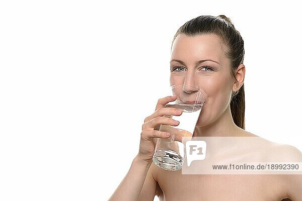 Lächelnde  hübsche  gesunde Frau  die ein Glas Wasser trinkt und in die Kamera schaut  vor weißem Hintergrund