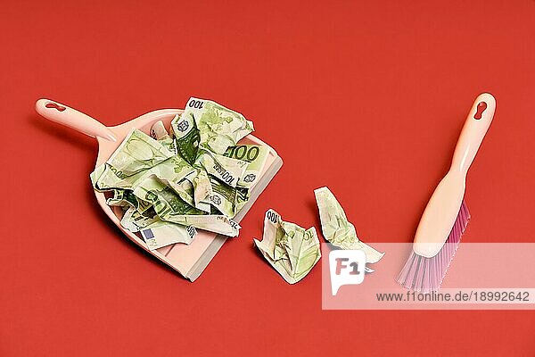 Kreatives Layout mit Kehrschaufel  Handbesen und zerknitterten Gelddollarscheinen auf rotem Hintergrund. Finanzen  Korruption  kriminelle Aktivität Konzept