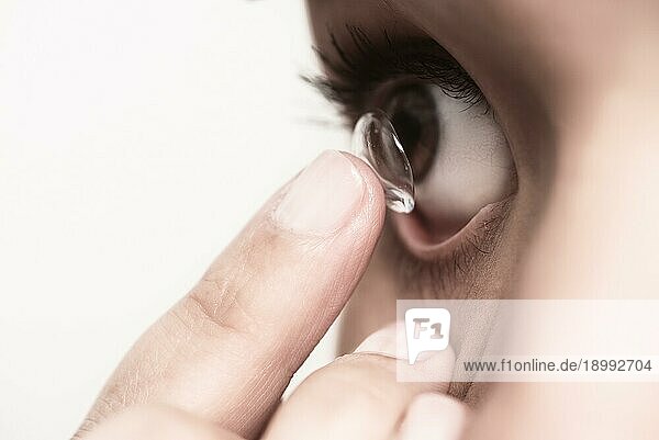 Frau  die eine Einweg Kontaktlinse aus Kunststoff in ihr Auge einsetzen will  um ihre Sehkraft zu korrigieren  balanciert diese auf dem Ende ihres Fingers vor ihrem Auge  wobei sie die Linse scharf stellt  extreme Nahaufnahme