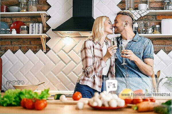 Junges glückliches Paar trinkt Champagner und genießt die Gesellschaft von einander in der Küche zu Hause. Beziehung  Feier Konzept