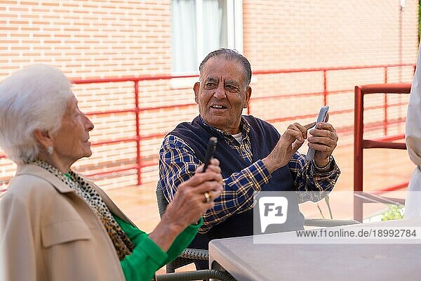 Zwei sehr glückliche ältere Menschen im Garten eines Pflegeheims  die auf das Telefon schauen  Technologien im Alter