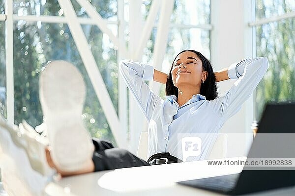 Attraktive afroamerikanische Geschäftsfrau ruht sich in einem modernen Büro aus und genießt ihre Freizeit. Entspannen Konzept. Pause Zeit