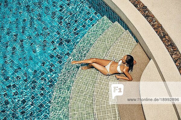 Draufsicht auf junge schlanke Frau in weißem Bikini entspannt im Schwimmbad. Sommerurlaub  Erholung Konzept
