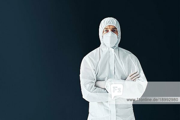 Selbstbewusster Arzt mit verschränkten Armen im medizinischen Schutzanzug mit Kopierraum auf schwarzem Hintergrund