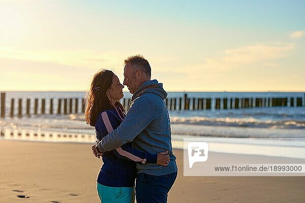 Romantisches Paar mittleren Alters  das sich an einem tropischen Strand bei Sonnenuntergang umarmt und sich liebevoll in die Augen schaut  mit seitlichem Kopierraum