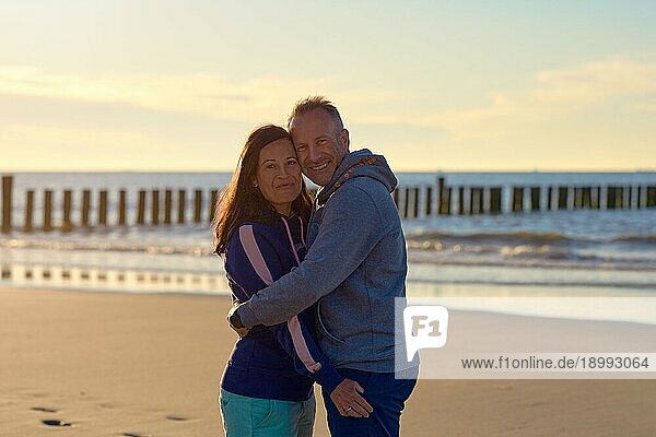 Glückliches romantisches Paar mittleren Alters genießt eine liebevolle Umarmung an einem verlassenen tropischen Strand bei Sonnenuntergang und lächelt in die Kamera mit Kopie Raum