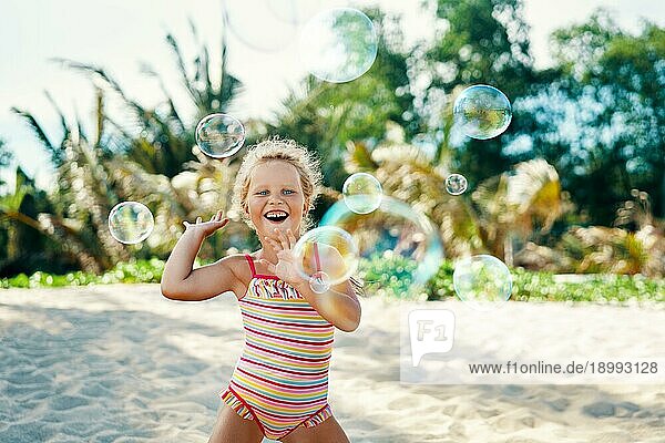 Kleines glückliches Mädchen spielt Seifenblasen am aktuellen Strand. Kind Spaß Konzept