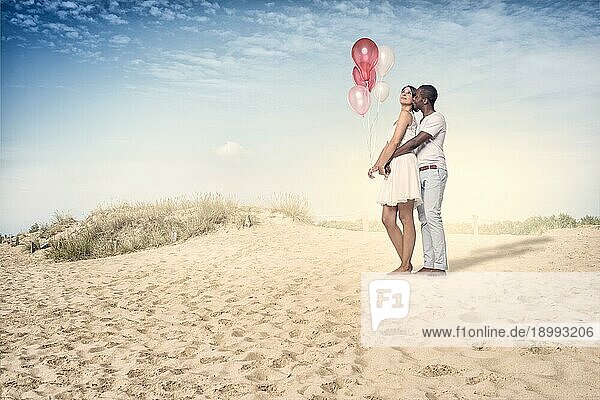 Süßes junges Paar am Strand mit Luftballons an einem sehr sonnigen Tag stehend