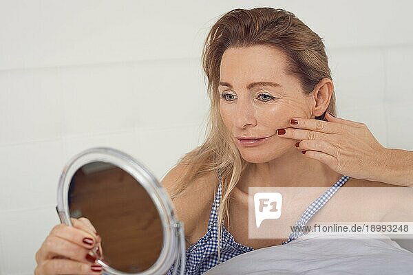 Porträt einer besorgten Frau  die über das Altern nachdenkt  während sie im Spiegel ihr Gesicht und ihre Gesichtsfalten betrachtet