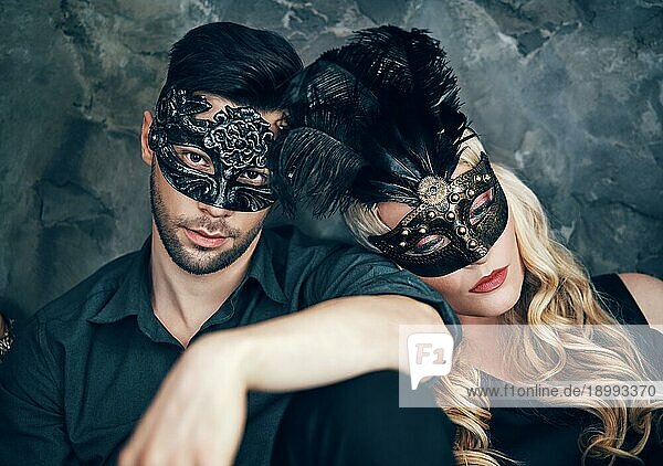Schönes Paar in geheimnisvollen schwarzen Maske sitzt auf dem Boden im Studio. Mode  Party Konzept