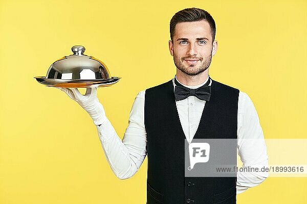 Handsome eleganten Kellner hält Tablett und cloche bereit zu dienen auf gelbem Hintergrund. Service  Restaurant  Horeca Konzept