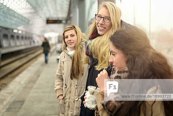 Attraktive junge Frauen unterschiedlicher Größe warten auf dem Bahnsteig eines modernen Pendlerbahnhofs im Freien auf einen Zug