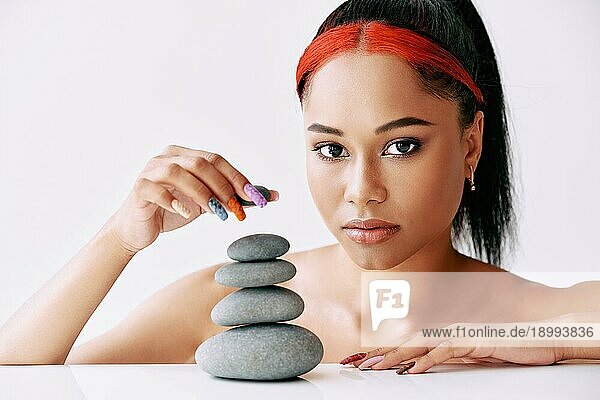 Hübsche afroamerikanische Frau macht Pyramide der Steine auf weißem Hintergrund. Balance Konzept