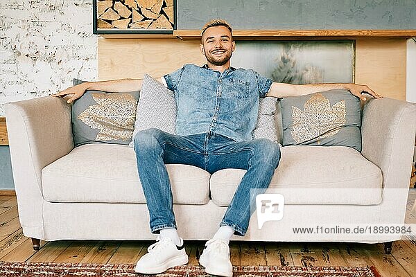 Hübscher lächelnder Mann entspannt sich auf dem Sofa zu Hause. Ruhe Konzept