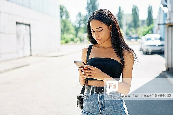 Schöne stilvolle schwarze Frau  die auf ihr Handy schaut  wenn sie in der Stadt spazieren geht
