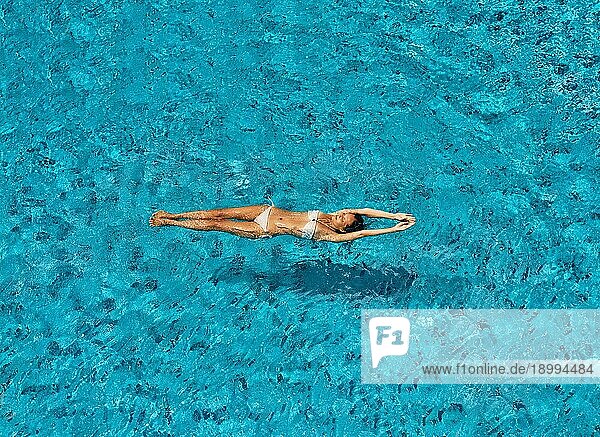 Draufsicht auf junge schlanke Frau in weißem Bikini entspannen und schwimmen in Infinity Pool. Sommerurlaub  Ruhe Konzept