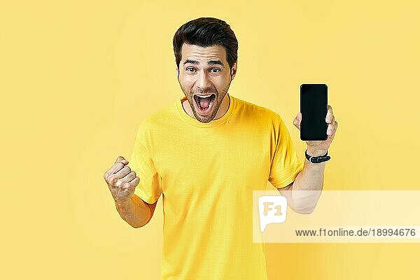 Aufgeregter  schreiender Mann  der sein Handy hält und in die Kamera schaut  in einem gelben Studiohintergrund. Kommunikation Konzept