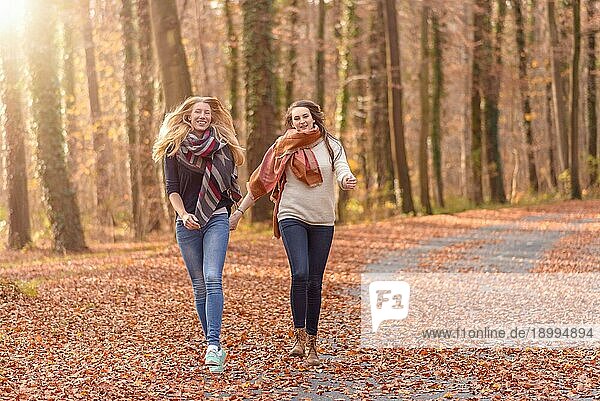 Zwei fröhliche Frauen  die Hand in Hand durch einen bewaldeten Herbstpark laufen  in dem bunte Blätter auf dem Boden liegen ein Konzept für einen gesunden Lebensstil