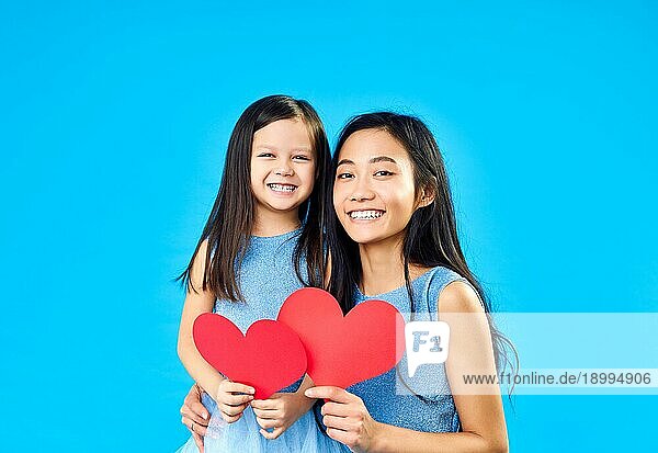 Lächelndes kleines Mädchen und ihre Mutter hält Papier Herz auf blauem Hintergrund. Glückliche Familie Liebe Konzept