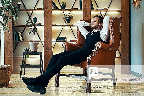 Selbstbewusster junger Mann entspannt sich im Sessel in luxuriösem Interieur. Erfolg und Ruhekonzept