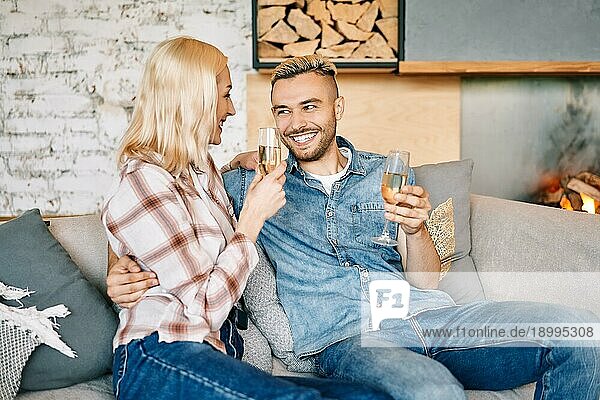 Junges glückliches Paar trinkt Champagner und lächelnd sitzt auf dem Sofa in ihrem modernen Haus. Beziehung  Feier  Dating Konzept