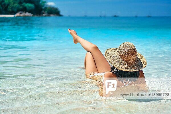 Rückenansicht der jungen Frau in Strohhut und weißem Bikini entspannen in türkisfarbenen Meer auf tropischen Paradies Strand. Sommerurlaub  Reiseziel  Urlaub Konzept