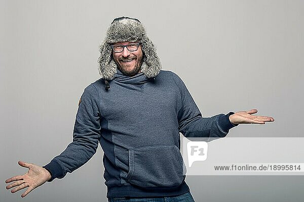 Fröhlicher Mann mit Brille und Wintermütze  jubelnd und feiernd  über grauem Hintergrund mit Leerzeichen
