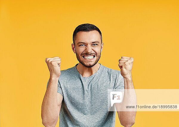 Glücklicher Mann feiert seinen Erfolg mit Gewinner Geste auf gelbem Hintergrund. Sieg  Triumph und Emotionen Konzept
