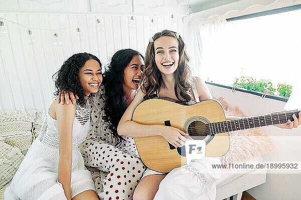 Lachen glücklich Frauen mit Gitarre haben Spaß zusammen im Inneren des Wohnmobils genießen Partei. Verschiedene Ethnien Frauen Freundschaft und Frauen Schönheit Konzept