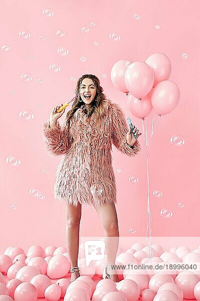 Junge hübsche Frau  die Spaß mit Seifenblasen auf rosa Hintergrund mit Luftballons. Party  Feier  Spaß Konzept