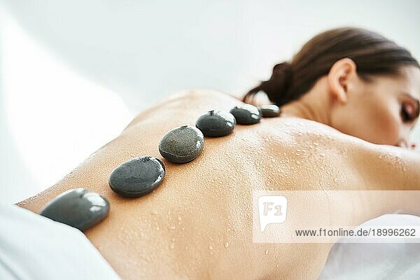 Junge Frau entspannt sich im SpaSalon mit heißen Steinen auf dem Rücken. Massage  Therapie  Schönheitsbehandlung Konzept